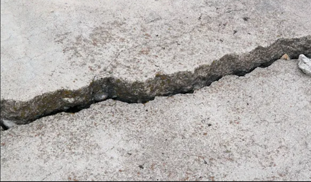 Wide crack with raised, uneven edges running across a concrete driveway