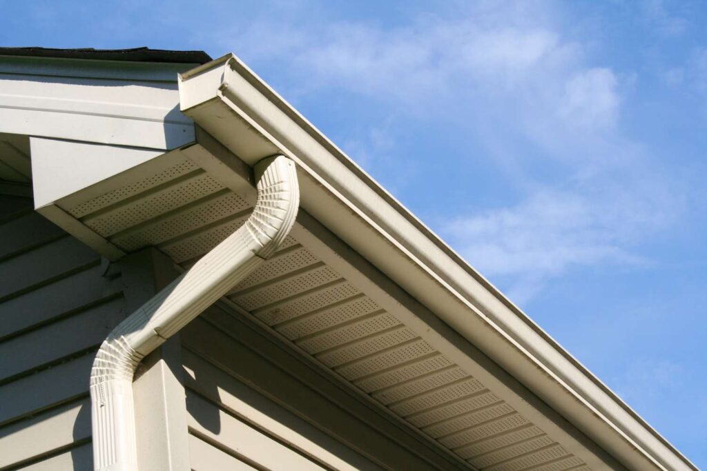 Gutter and downspout at the corner of a house roofline seen from below