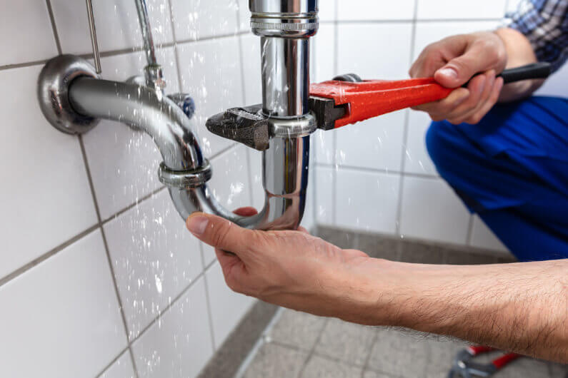 Plumber tightening a leaking chrome sink drain pipe with a wrench